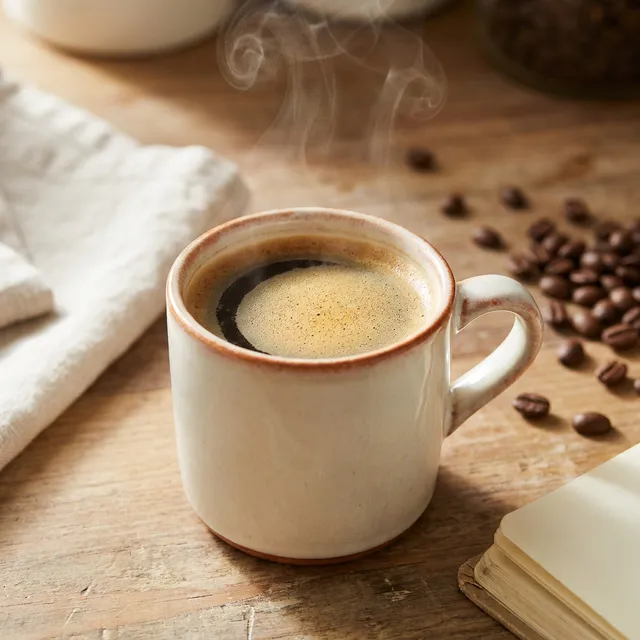 Stoneware mug of freshly brewed black coffee steaming on a wooden kitchen counter