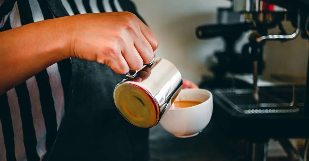 Barista pouring steamed milk into a coffee cup.