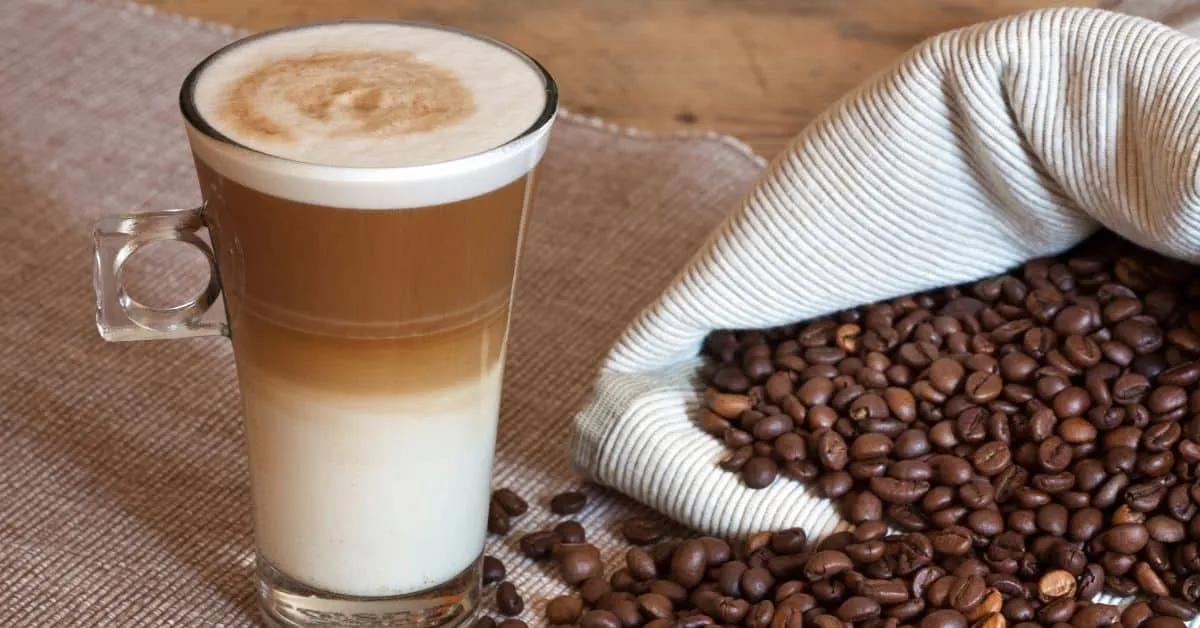 Cafe Latte standing on a table in front of coffee beans.