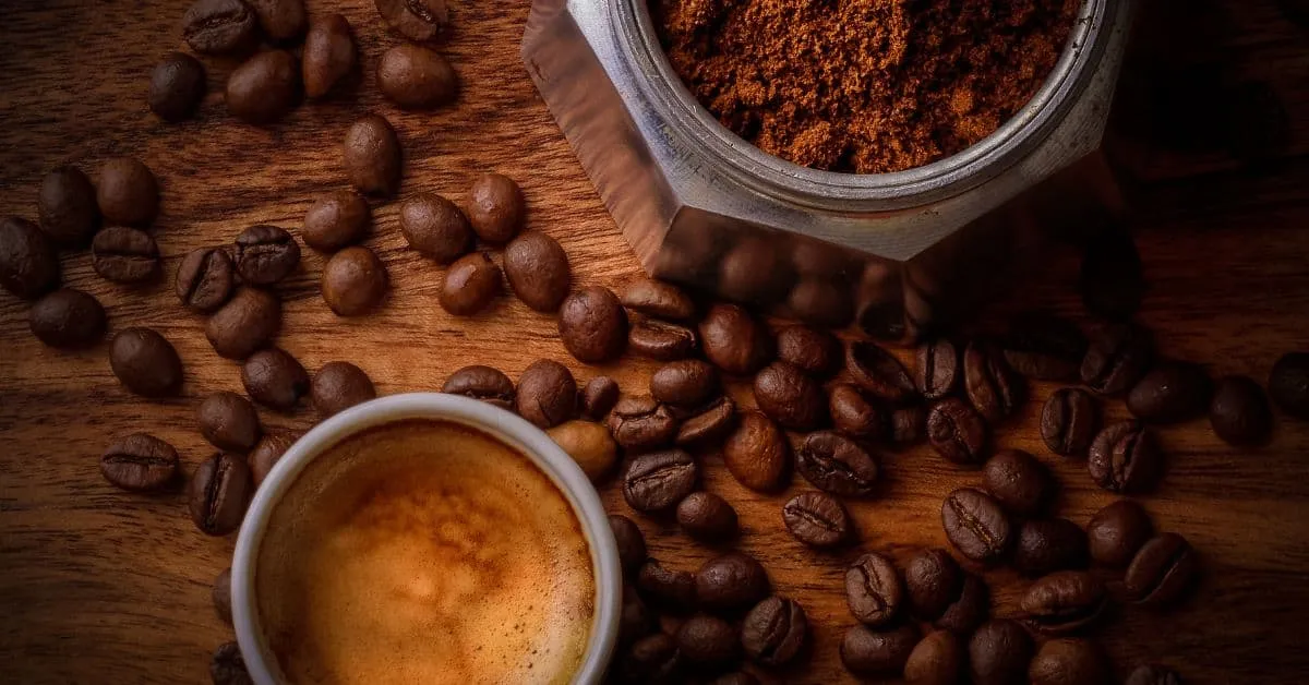 A mug of coffee on a table next to espresso beans.