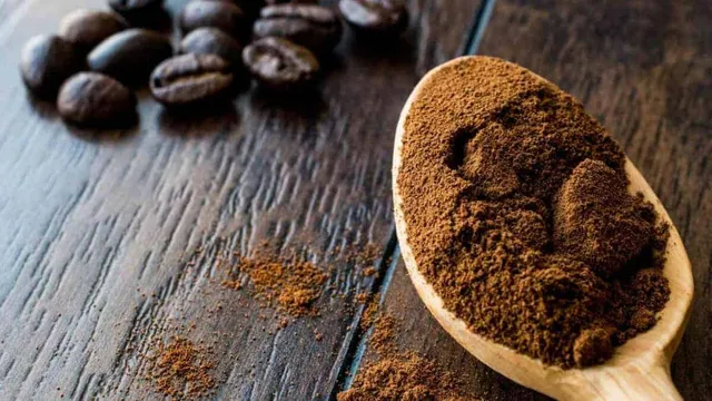 A wooden spoon heaped with dark instant espresso powder beside whole roasted coffee beans